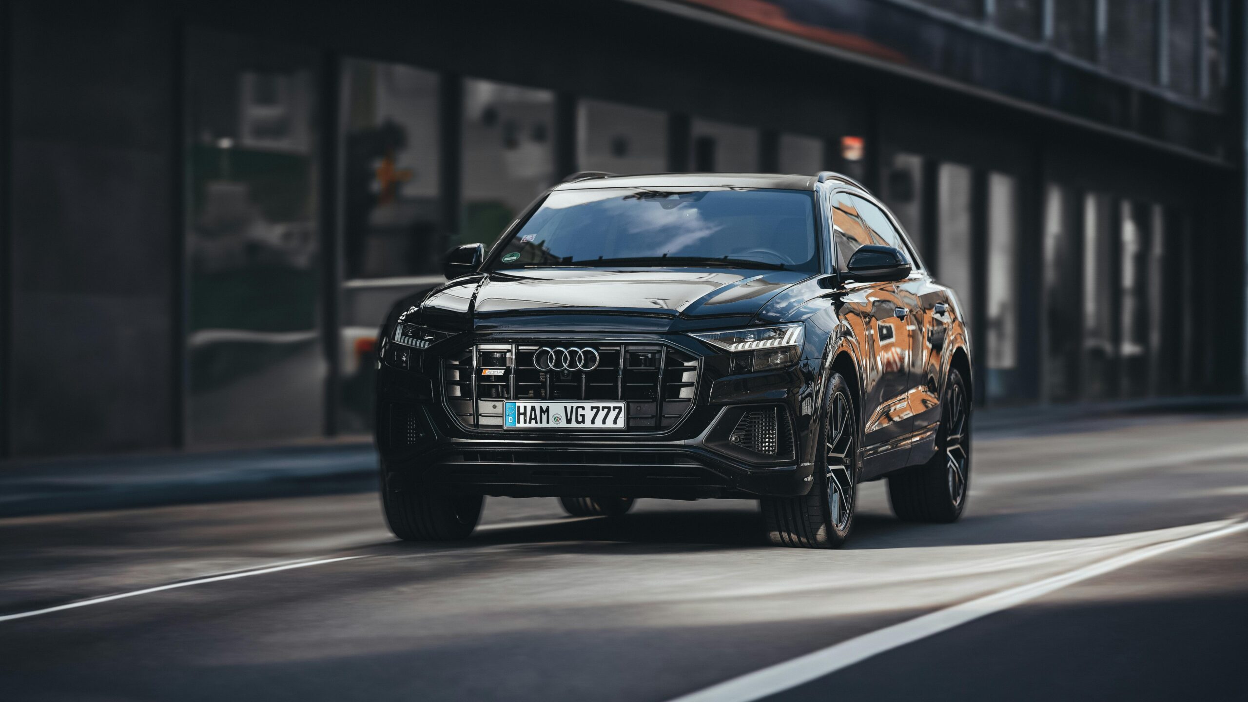Black Audi Q8 SUV driving through city streets with modern architecture background.